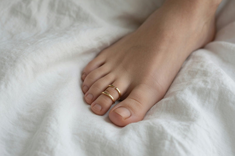 Gold adjustable open-band toe rings on a second toe, showing the gap used to stop spinning and sliding